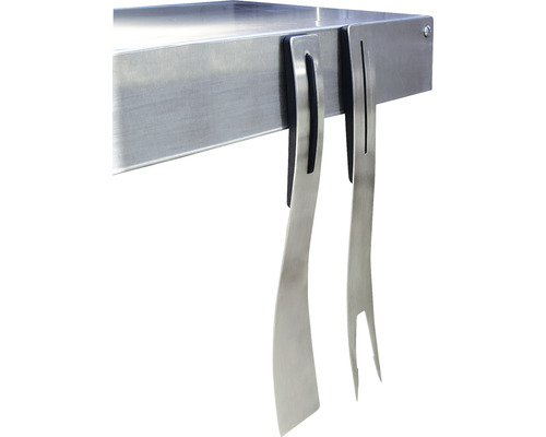 Grilovací příslušenství, jako je kovová obracečka a vidlice, zavěšené na grilovacím stole.