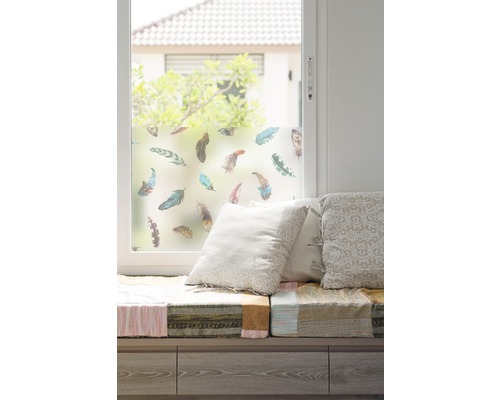 Okno s okenní fólií a motivem peří, lavice s polštáři.