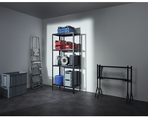 Fotografie suterénu s regálem obsahujícím krabice, bedny na nářadí, kabelový buben a kbelík, dále žebřík, dvě šedé skládací krabice a tapetovací stůl.