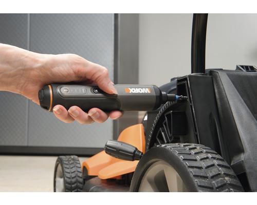 Ruka drží akumulátorový šroubovák, který se používá na sekačce na trávu.