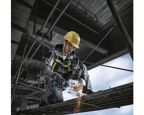 Stavební dělník s ochrannou přilbou používá úhlovou brusku na lešení.