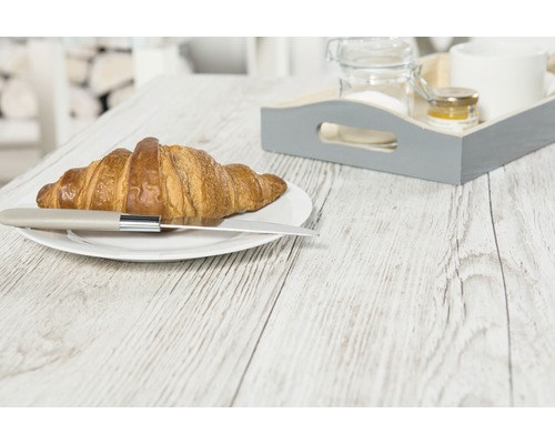 Croissant s nožem na talíři a snídaňový tác na dřevěném stole.