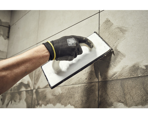 Obkladač nanáší spárovací hmotu na dlaždice pomocí hladítka