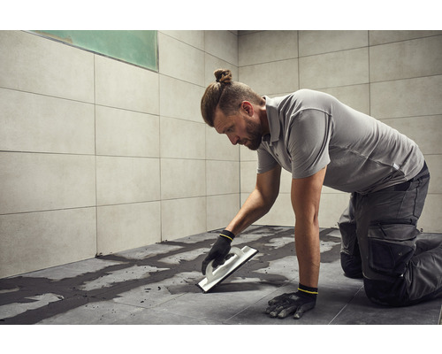 Muž spáruje dlaždice v koupelně pomocí spárovací gumy.