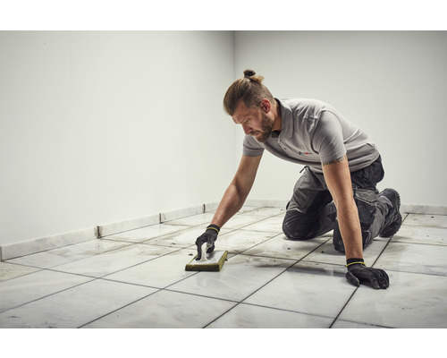 Dlaždič čistí dlaždice pomocí houbového hladítka