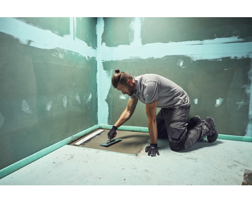 Řemeslník opracovává podlahovou plochu v koupelně hladítkem pro renovační práce