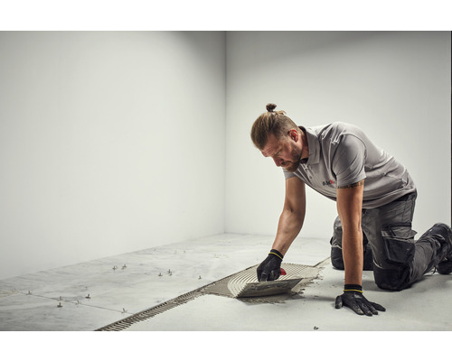 Obkladač nanáší lepidlo na dlaždice pomocí lžíce.