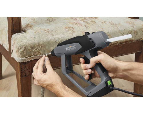 Osoba připevňuje okraj ke židli pomocí tavné pistole.