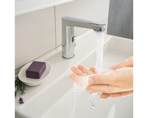 Osoba si myje ruce pod chromovanou vodovodní baterií v umyvadle.