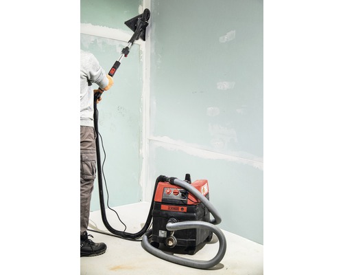 Osoba brousí stěnu s bruskou na sádrokarton a vysavačem.