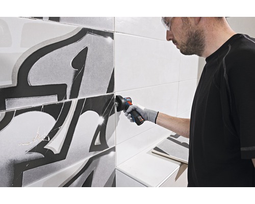 Řemeslník opracovává dlaždice úhlovou bruskou v koupelně.