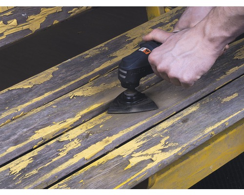 Osoba používá multifunkční nástroj k broušení barvy na dřevěné lavici.