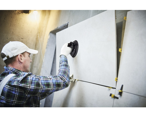 Obkladač pokládá dlaždice na zeď pomocí přísavného nástroje