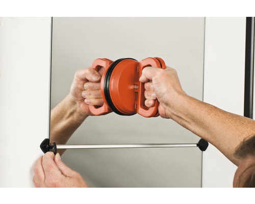 Osoba montuje zrcadlo na zeď pomocí přísavky