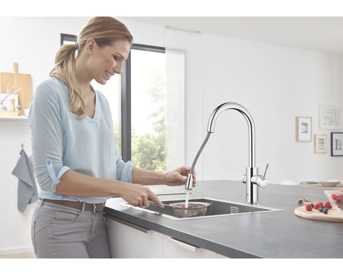 Žena oplachuje bobule v sítu pod kuchyňskou baterií s výsuvnou sprchou.