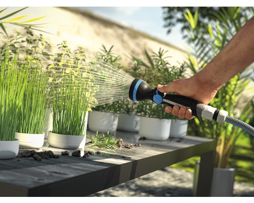 Osoba zalévá rostliny v květináčích zahradní stříkačkou na stole.