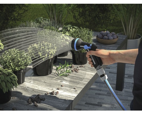Ruka zalévá rostliny zahradním postřikovačem na stole venku.