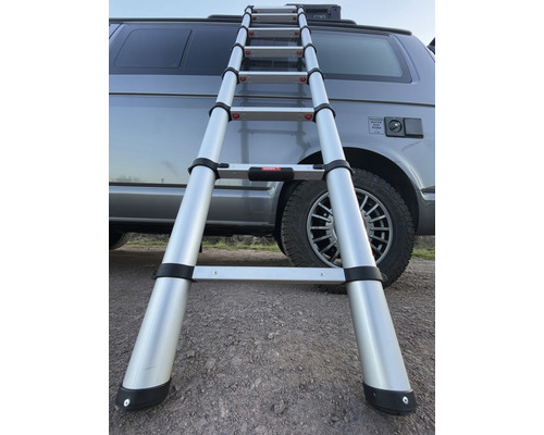 Rozložený teleskopický hliníkový žebřík před obytným vozem.