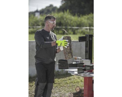 Muž s ochrannými brýlemi, pracovními rukavicemi a štípačkou na dřevo zpracovává dřevo