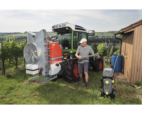 Muž čistí traktor vysokotlakým čističem ve venkovském prostředí.
