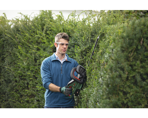 Muž stříhá živý plot akumulátorovými nůžkami na živý plot na zahradě.