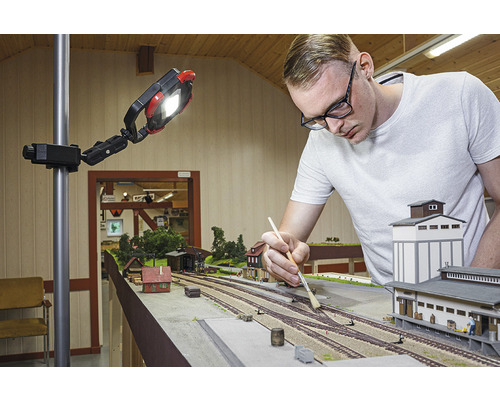 Muž pracuje na modelové železnici pod pracovním světlem.