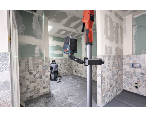 Pracovník používá čárový laserový nivelační přístroj se stativem v koupelně s obklady.