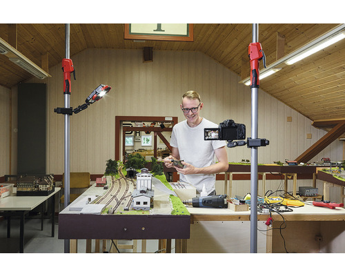 Muž natáčí modelovou železnici kamerou na stativu a pracovním světlem.