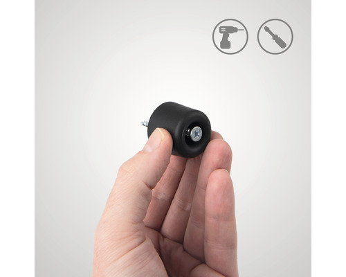 Ruka drží černý dveřní doraz pro montáž pomocí šroubu. Instalační symboly v pozadí.