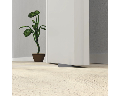 Šedý gumový dveřní klín umístěný před dveřmi.