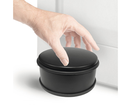 Černý kulatý dveřní zarážka vedle dveří s rukou na něm