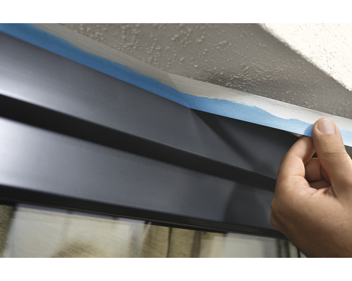 Maskování okenní tabule malířskou páskou před malováním.