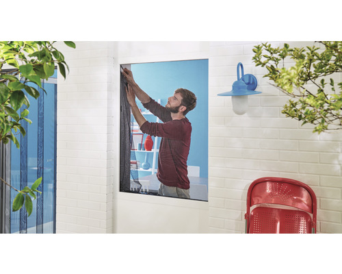 Muž montuje na okno síť proti hmyzu