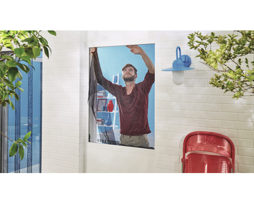 Muž montuje síť proti hmyzu na okno.