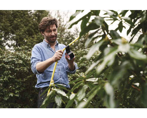 Muž opravuje žlutou zahradní hadici izolační páskou na zahradě.