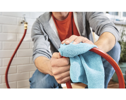 Muž čistí zahradní hadici hadříkem.