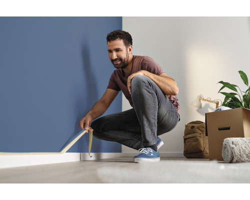 Muž lepí maskovací pásku na zeď v místnosti