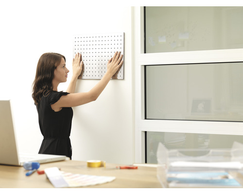 Žena upevňuje děrovaný panel na stěnu v kanceláři.