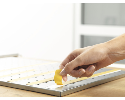 Ruka připevňuje lepicí pásku na kovový povrch.