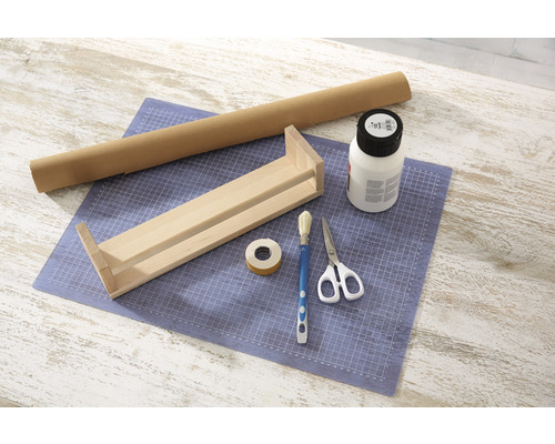 Pracovní stůl s dřevěnou policí, rolí papíru, lepidlem, štětcem, lepicí páskou a nůžkami