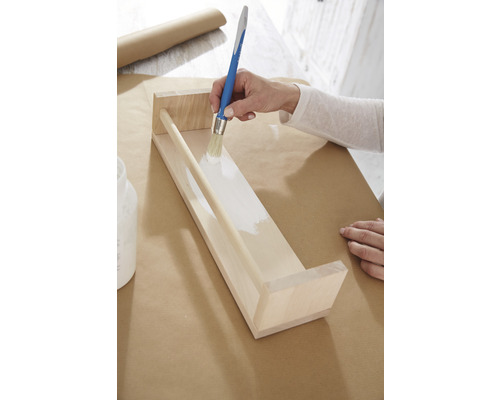 Osoba natírá dřevěnou polici bílou barvou štětcem.