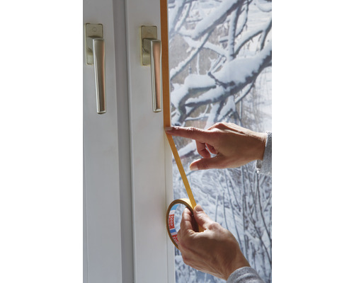 Osoba aplikuje těsnicí pásku na okenní rám.