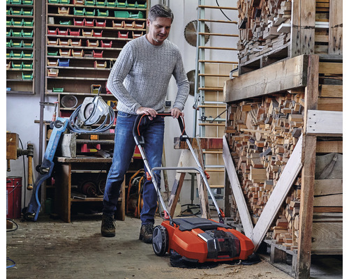 Muž používá akumulátorový zametač v dílně k úklidu pilin.