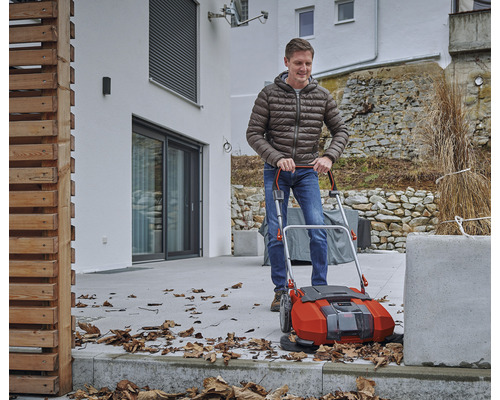 Muž používá venkovní zametač k odstraňování listí.