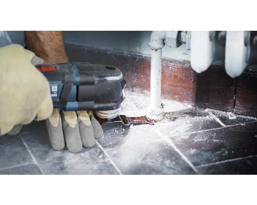 Osoba používá multifunkční nástroj na topné trubce poblíž zdi.