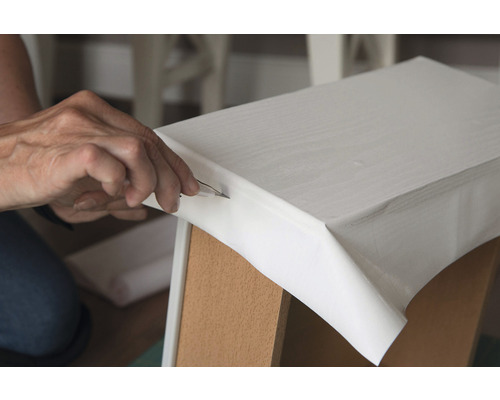 Osoba ořezává fólii na kusu nábytku modelářským nožem.