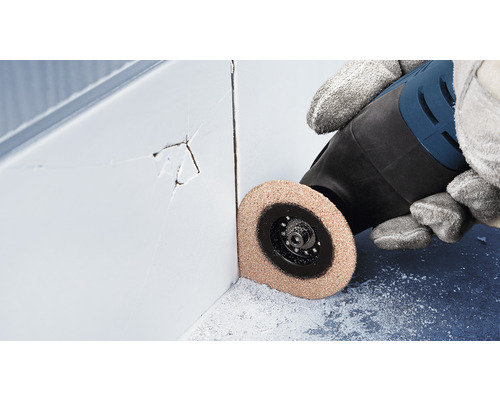 Osoba používá multifunkční nástroj k odstranění poškozených spár dlaždic.