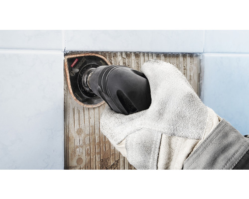 Ruka s ochrannou rukavicí odstraňuje dlaždice pomocí multifunkčního nástroje