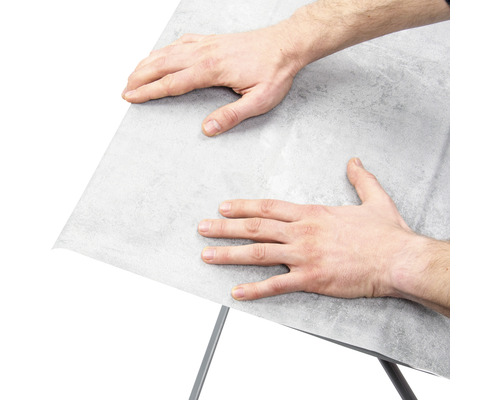 Muž připevňuje nábytkovou fólii na povrch.