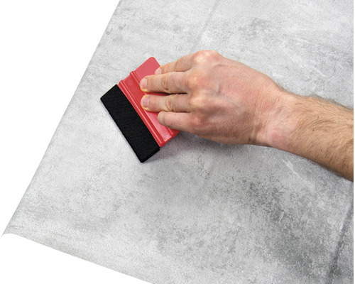 Ruka s raklí nanáší fólii s kamenným vzorem